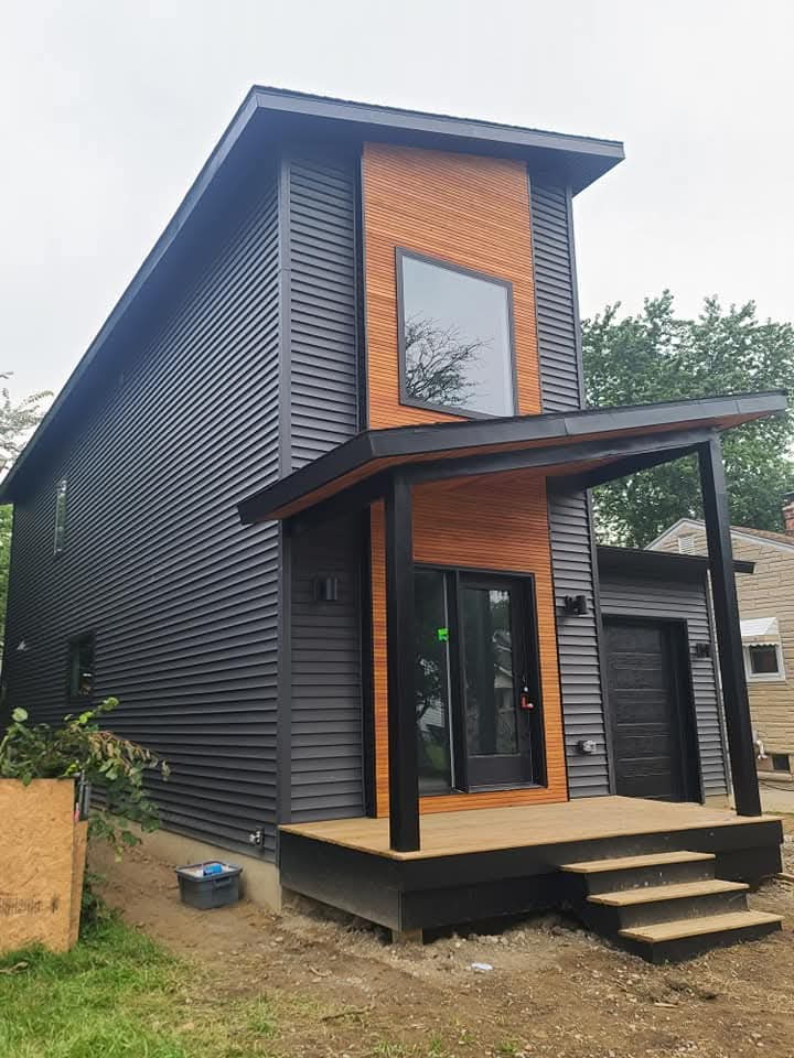 Renovated home with dark siding, warm wood accents and a covered front porch